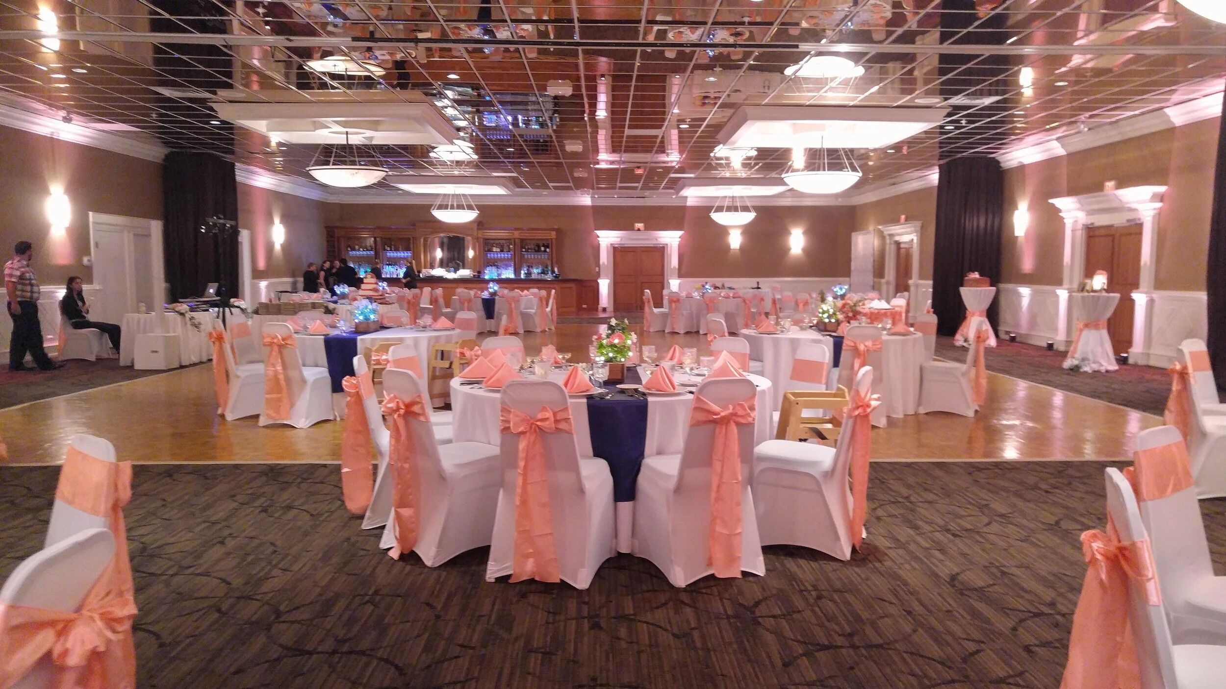 A banquet hall with round tables, white chairs with peach sashes, and a central floral arrangement.