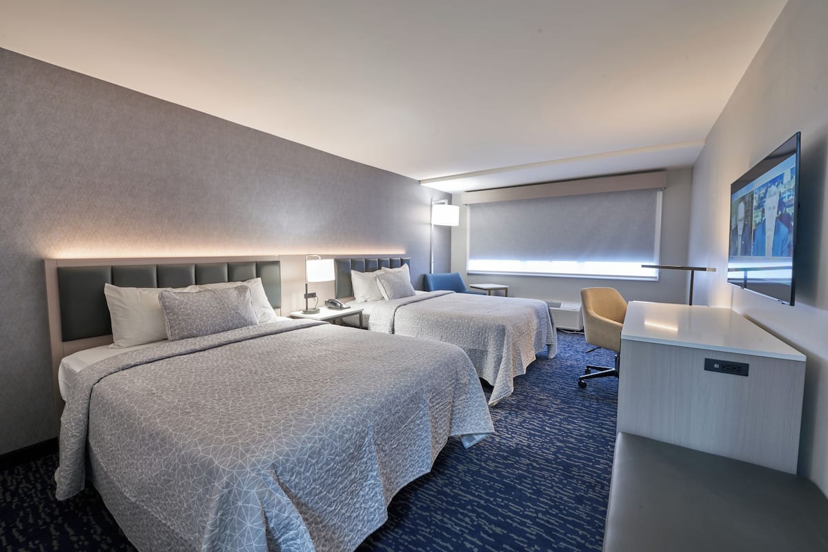 A hotel room with two beds, a desk, a chair, a TV, and a large window.