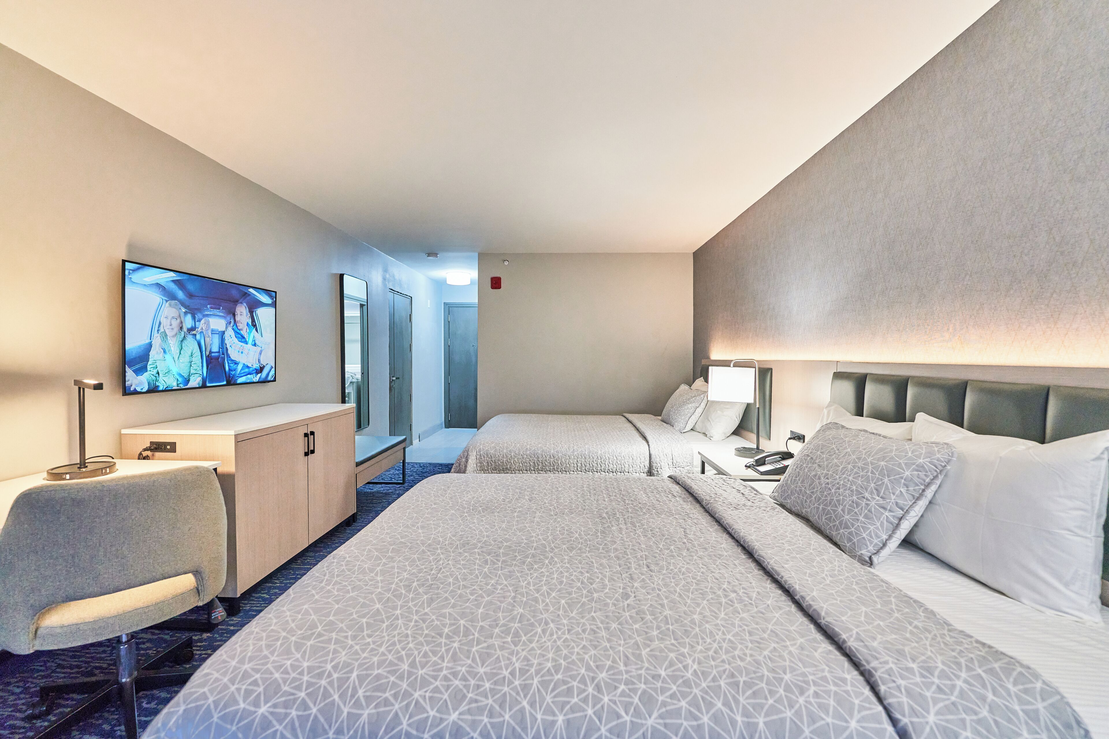 A hotel room with two beds, a desk, a TV, and a chair.