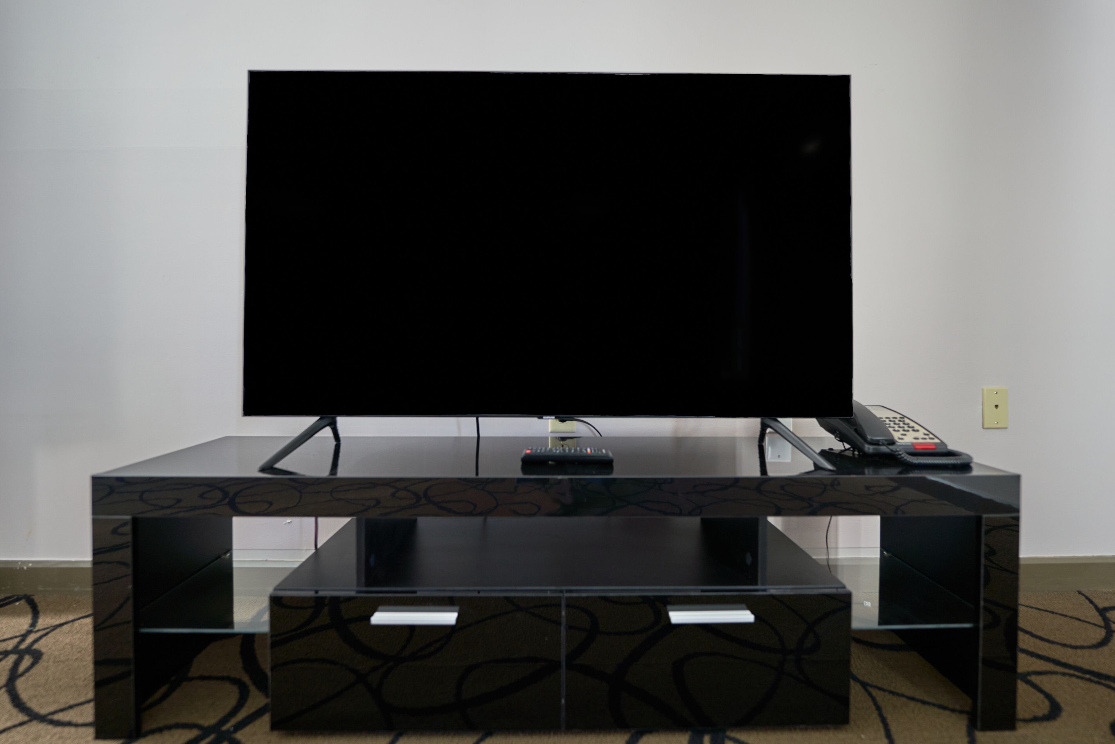 Un mueble multimedia negro con un televisor de pantalla plana, un teléfono y un control remoto.