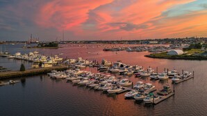 A marina with numerous boats docked, a distant cityscape, and a sunset sky. - Seaport Resort & Marina (Fairhaven)