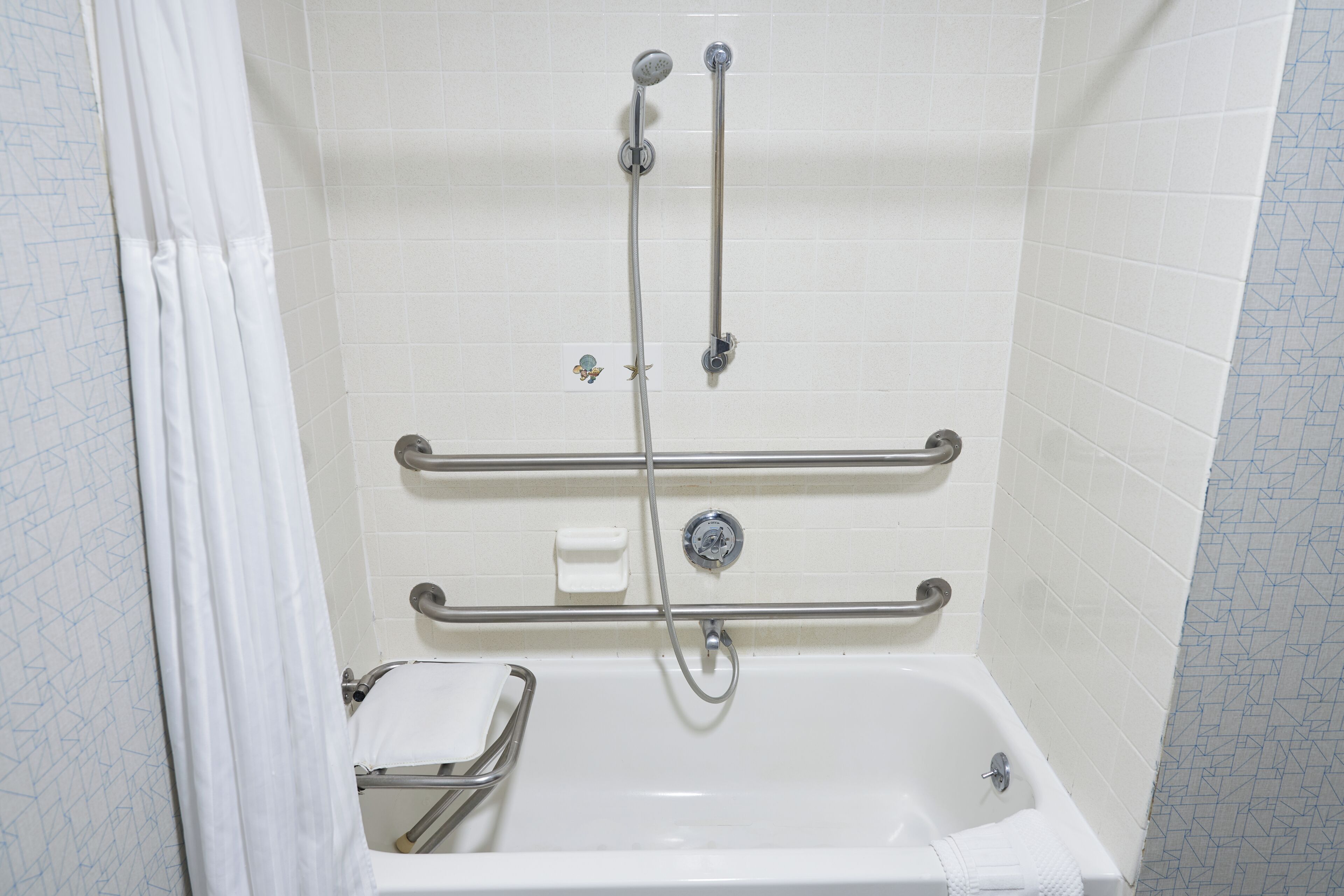 A walk-in shower with a grab bar, a handheld showerhead, and a handheld faucet.