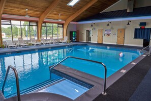An indoor swimming pool with clear water, a diving board, and lounge chairs.