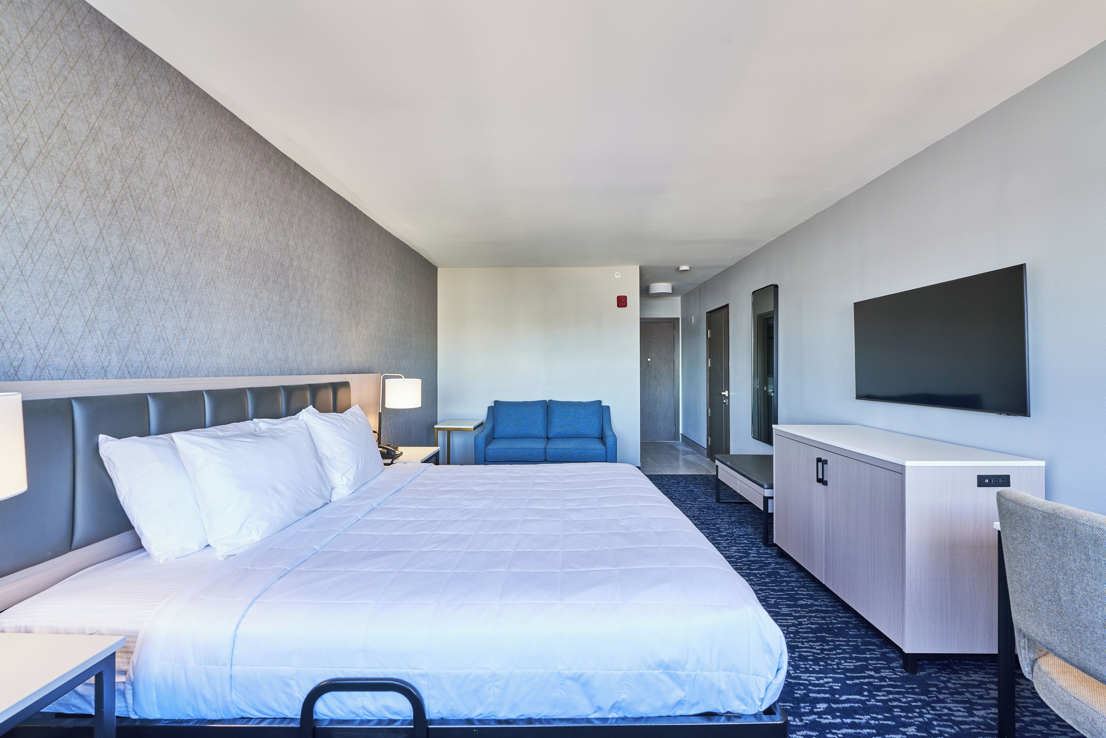 Una habitación de hotel con cama, escritorio, silla, televisor y zona de estar.