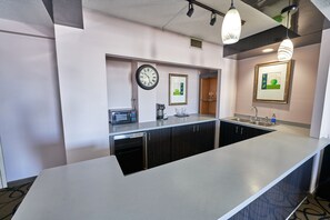 A modern kitchen with a built-in dishwasher, a microwave, and a sink. There are framed pictures on the wall and a clock above the sink.