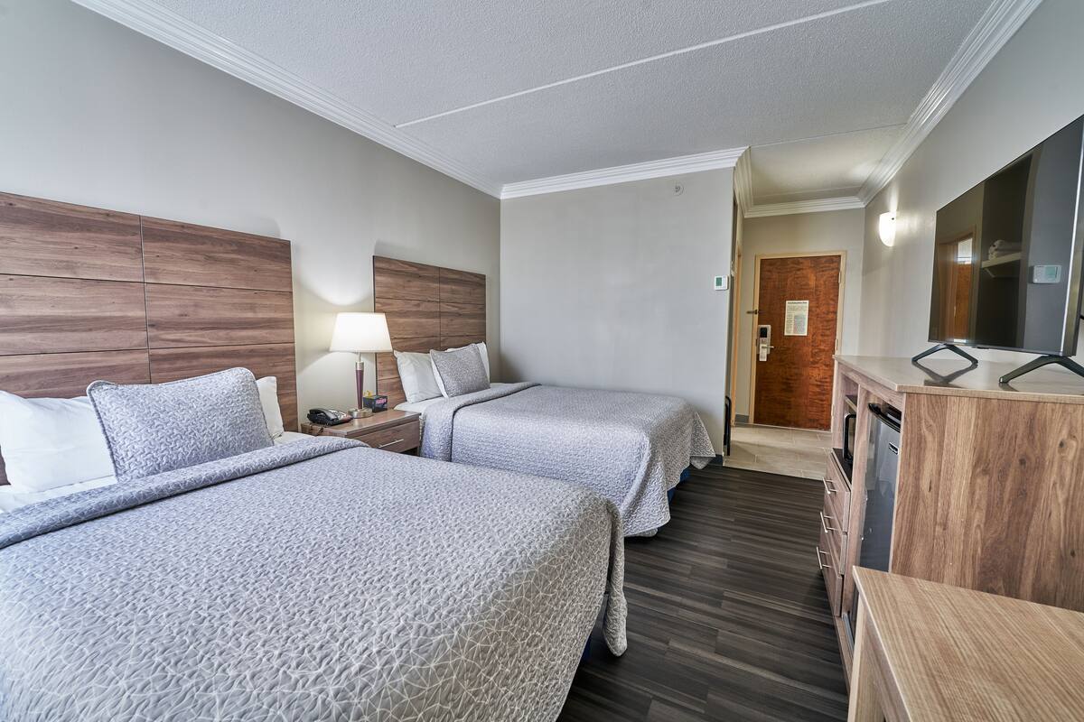 A hotel room with two beds, a wooden headboard, a desk with a lamp, and a mirror.