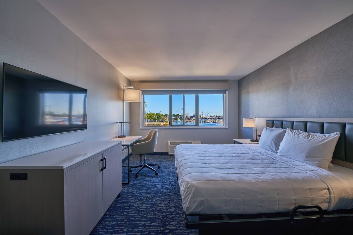 A hotel room with a bed, desk, chair, TV, and a large window with a view.