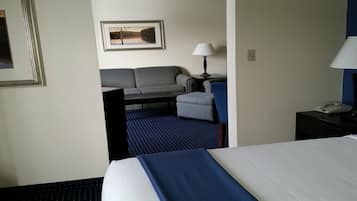 Ett hotellrum med en säng, ett skrivbord, en stol, en lampa och en inramad tavla på väggen.