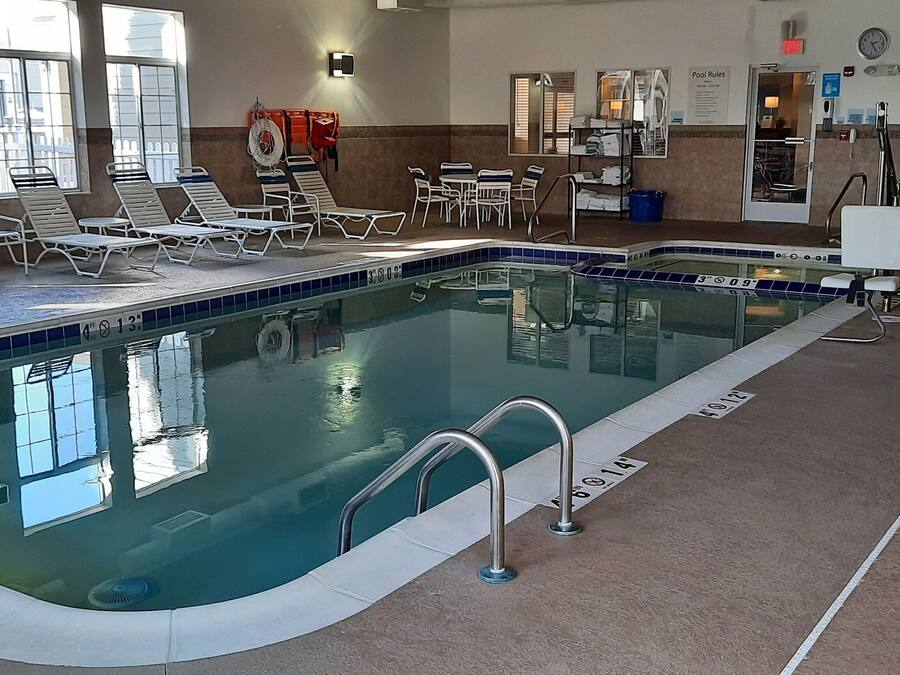 Una piscina interior con sillas de descanso y mesas, señalización clara de las normas de la piscina y un puesto de socorristas.