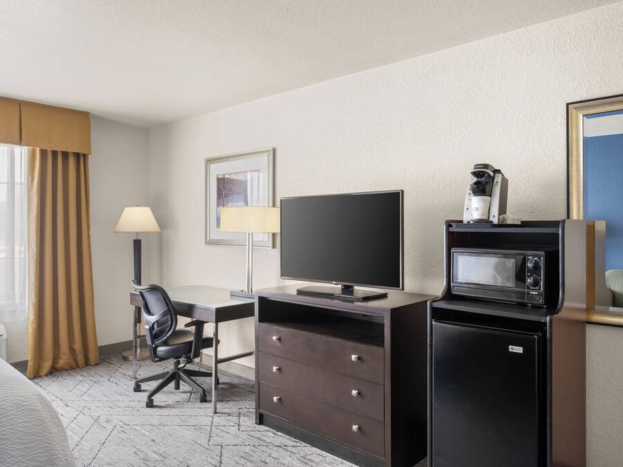 A hotel room with a bed, a desk with a chair, a television, a microwave, and a coffee maker.