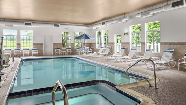 Piscina interior com água azul cristalina, rodeada por espreguiçadeiras e um guarda-sol.
