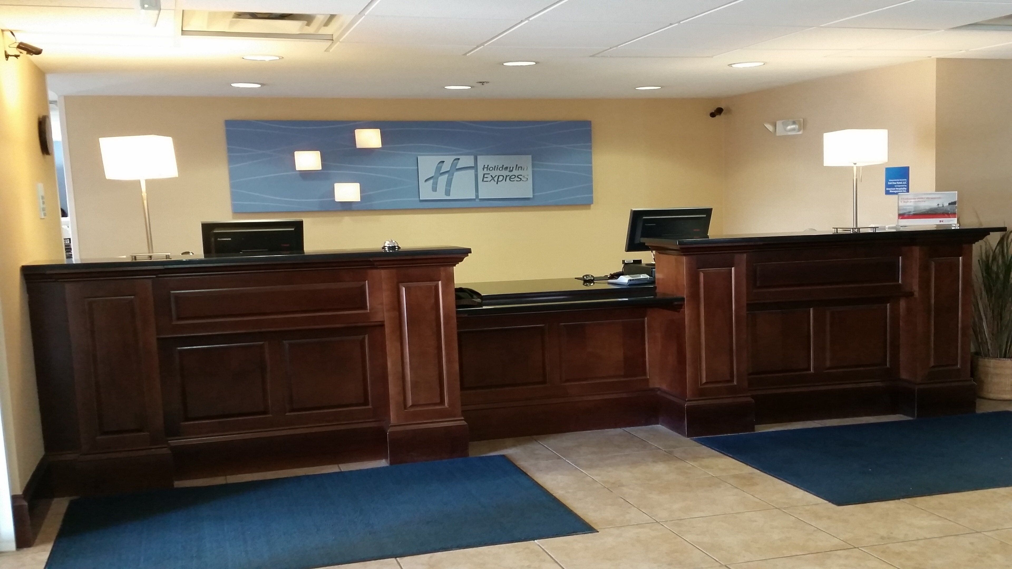 A reception desk with a blue carpet, a wall-mounted sign, and a potted plant.