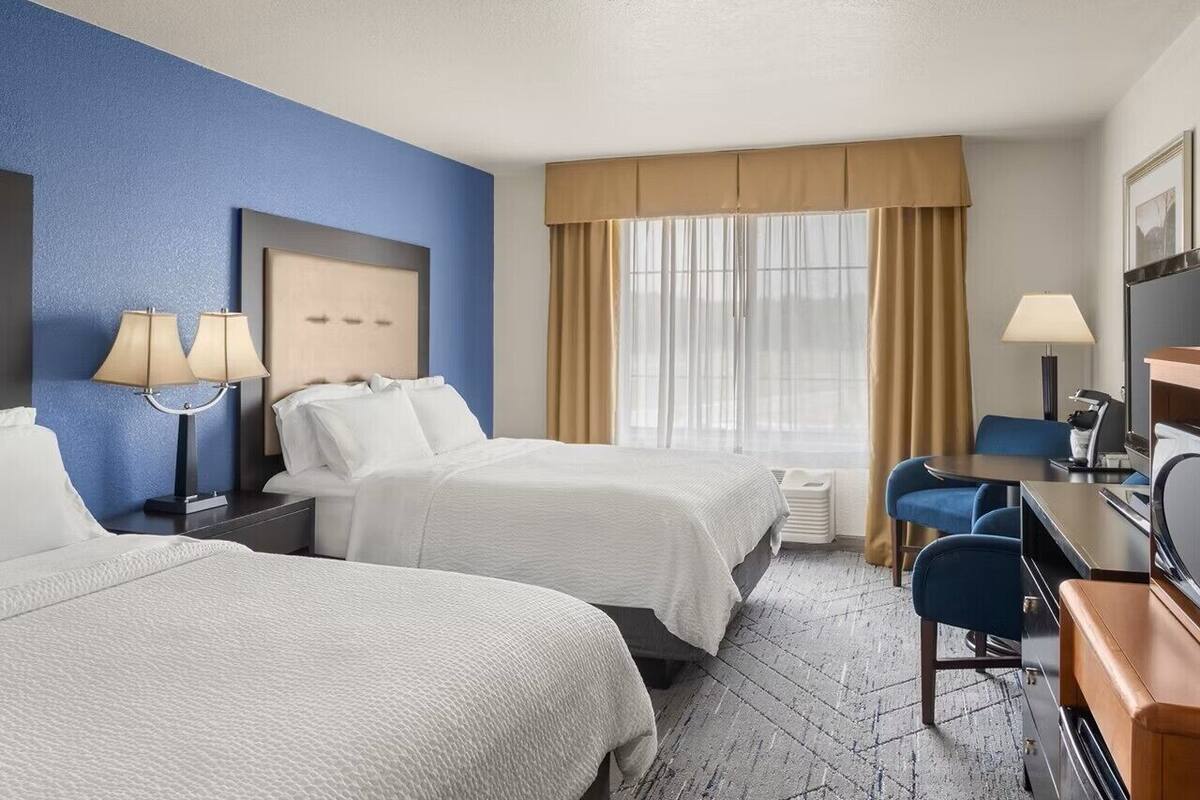 A hotel room with two beds, a desk, a chair, and a TV.
