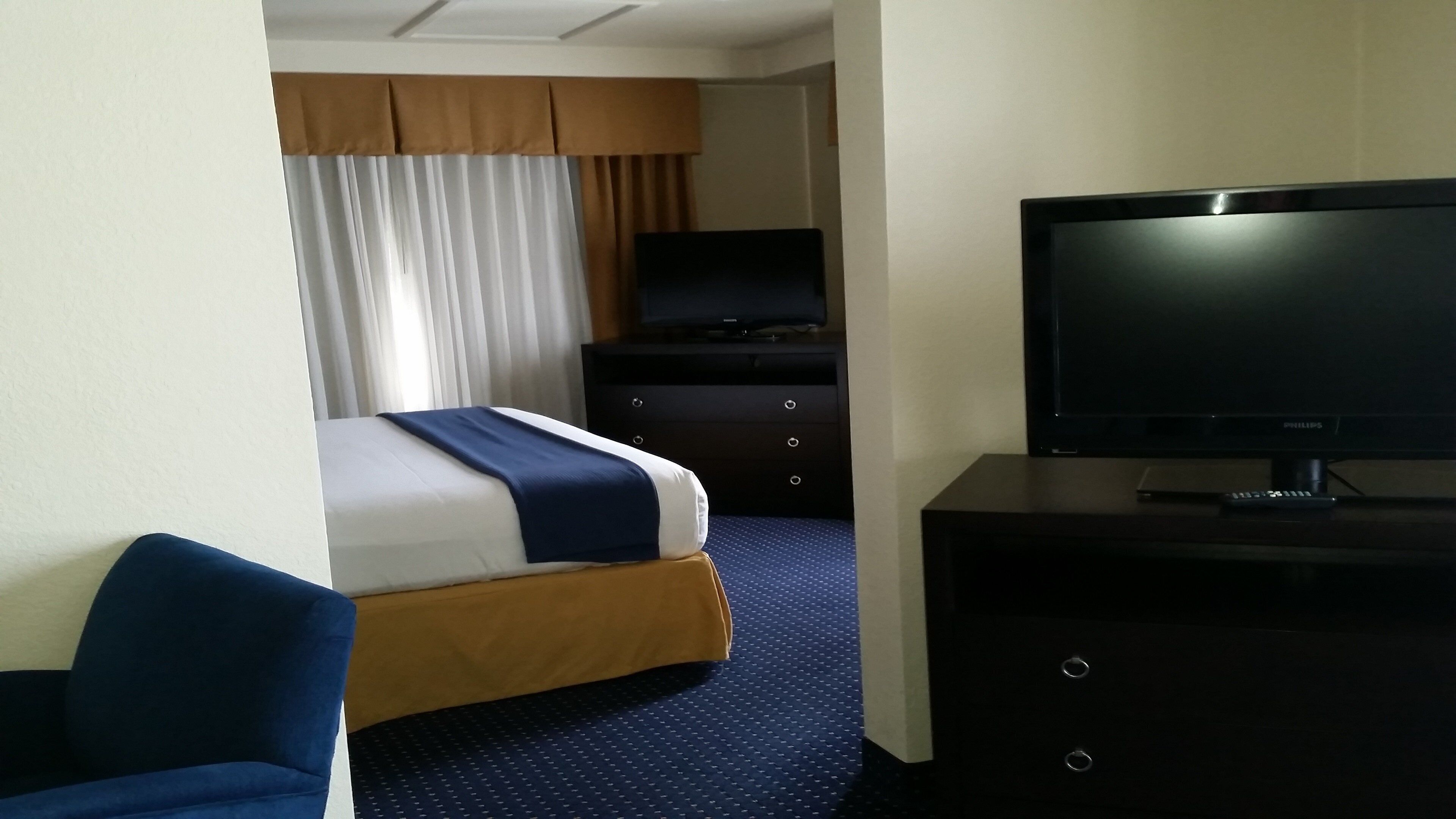 Une chambre d’hôtel avec un lit, une télévision, une commode et une chaise.