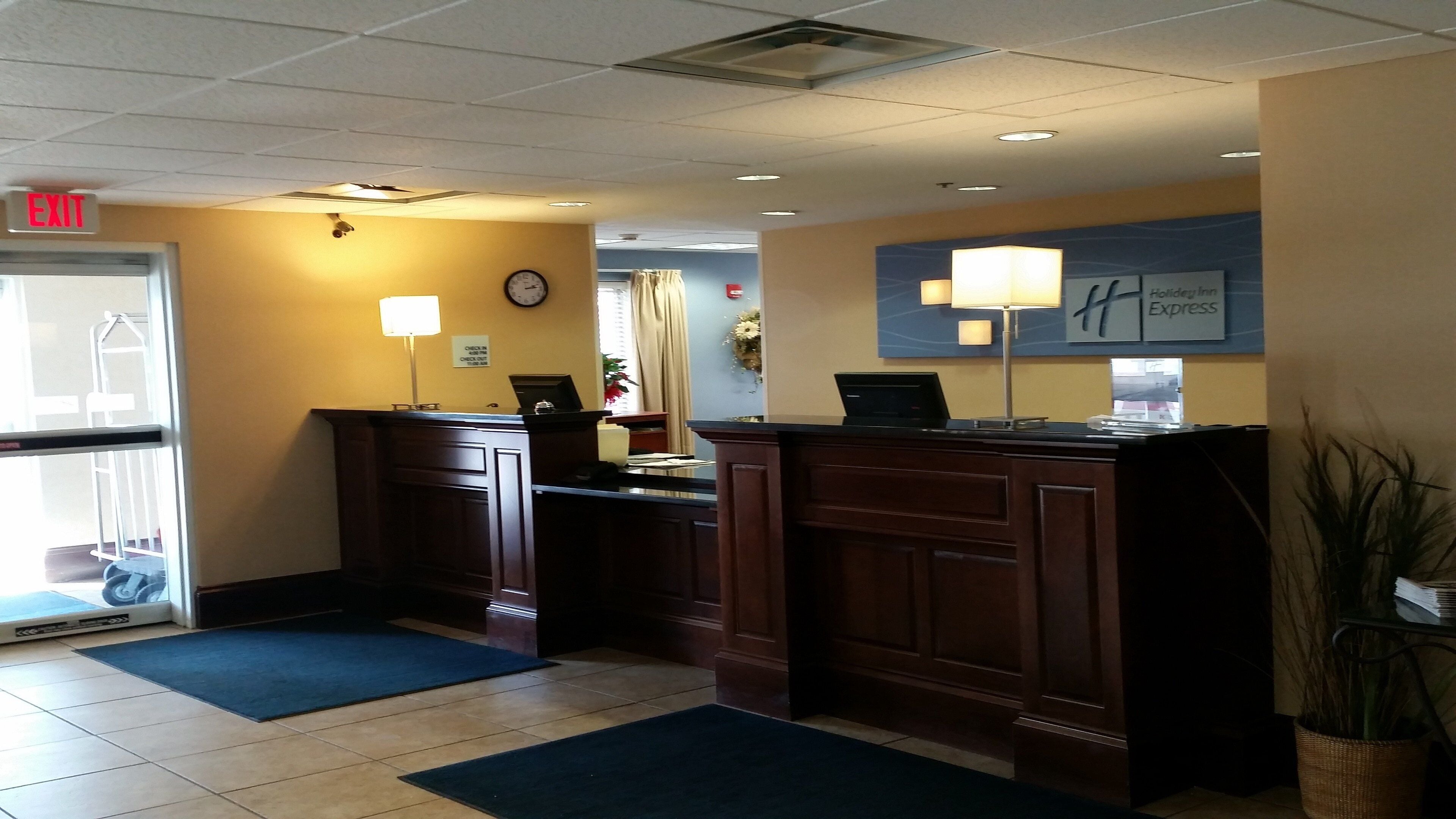 A hotel reception area with a reception desk, a clock, a sign for the Holiday Inn Express, and a plant.