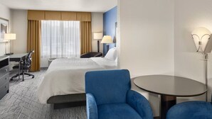 Quarto de hotel com cama, escrivaninha, cadeira, mesa redonda e abajur.