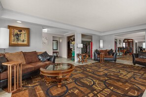 A spacious living room with a brown patterned carpet, a glass coffee table, and two sofas with leather cushions.