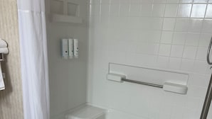 A modern bathroom with a walk-in shower, white tiles, a handrail, and a towel rack.