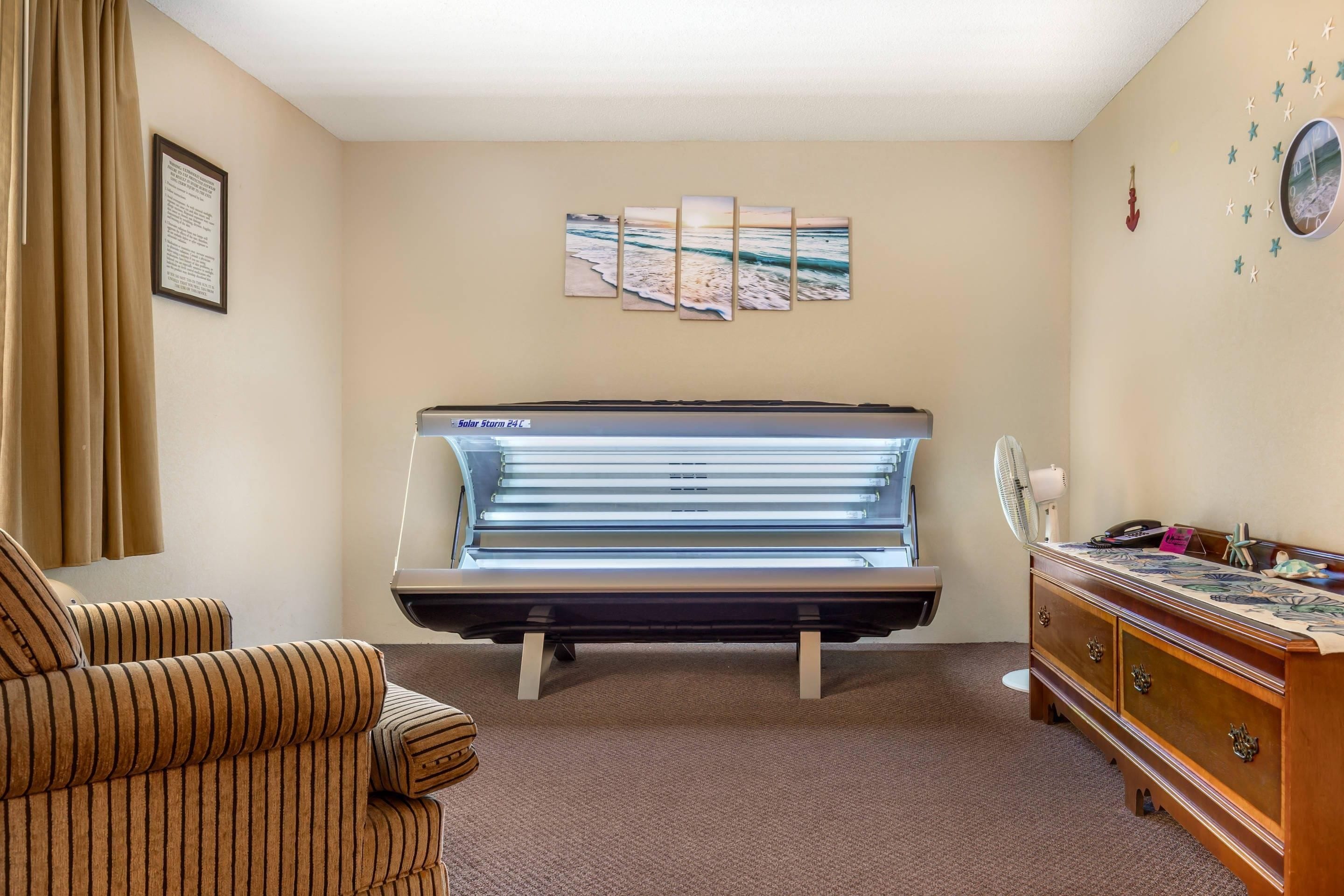 A room with a tanning bed, a chair, a dresser, and wall art.