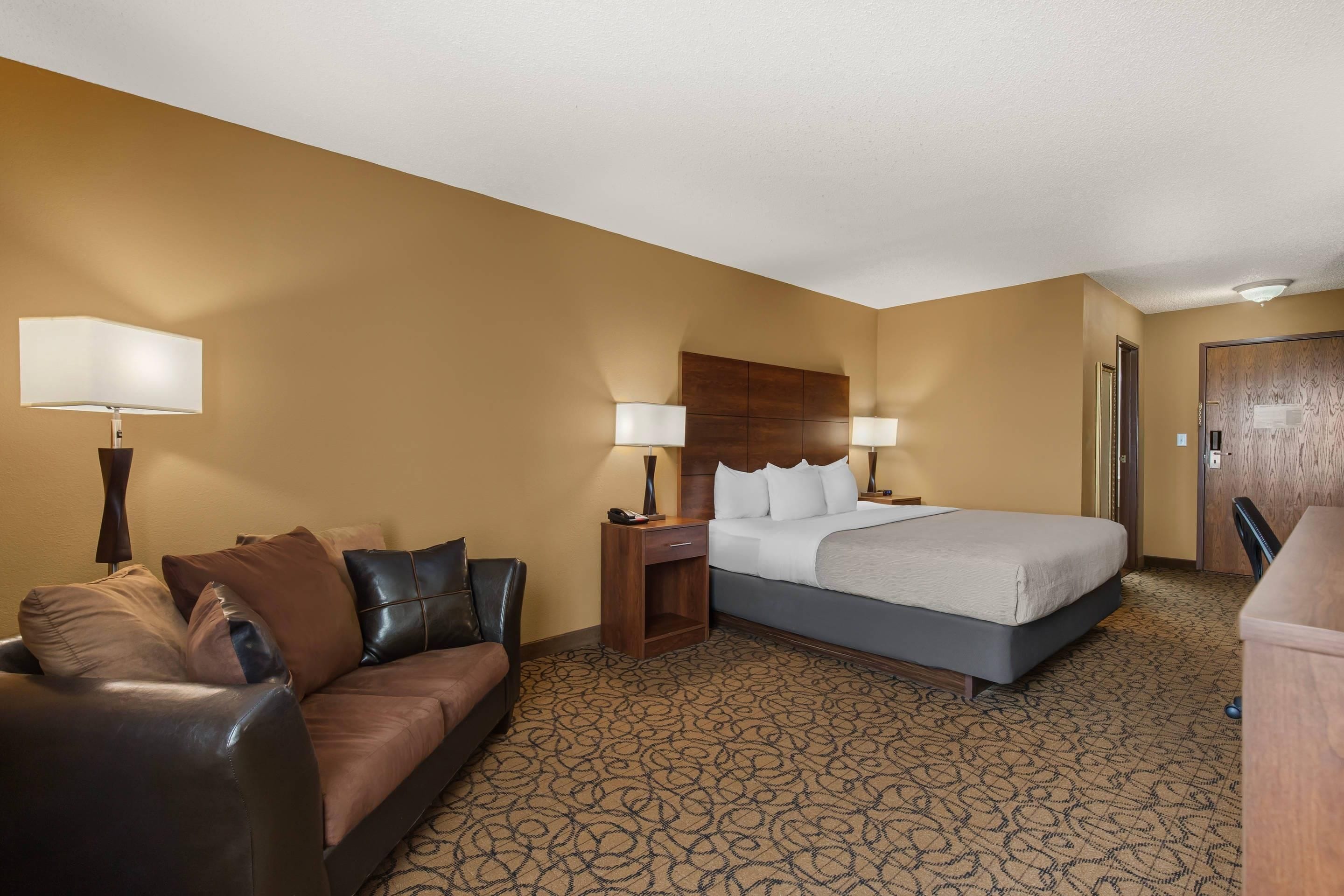A hotel room with a bed, a sofa, a nightstand, and a lamp.