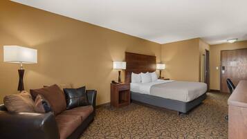 A hotel room with a bed, a sofa, a nightstand, and a lamp.