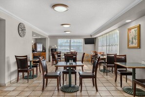 A hotel dining area with multiple tables and chairs, a clock on the wall, and a television mounted on the wall.