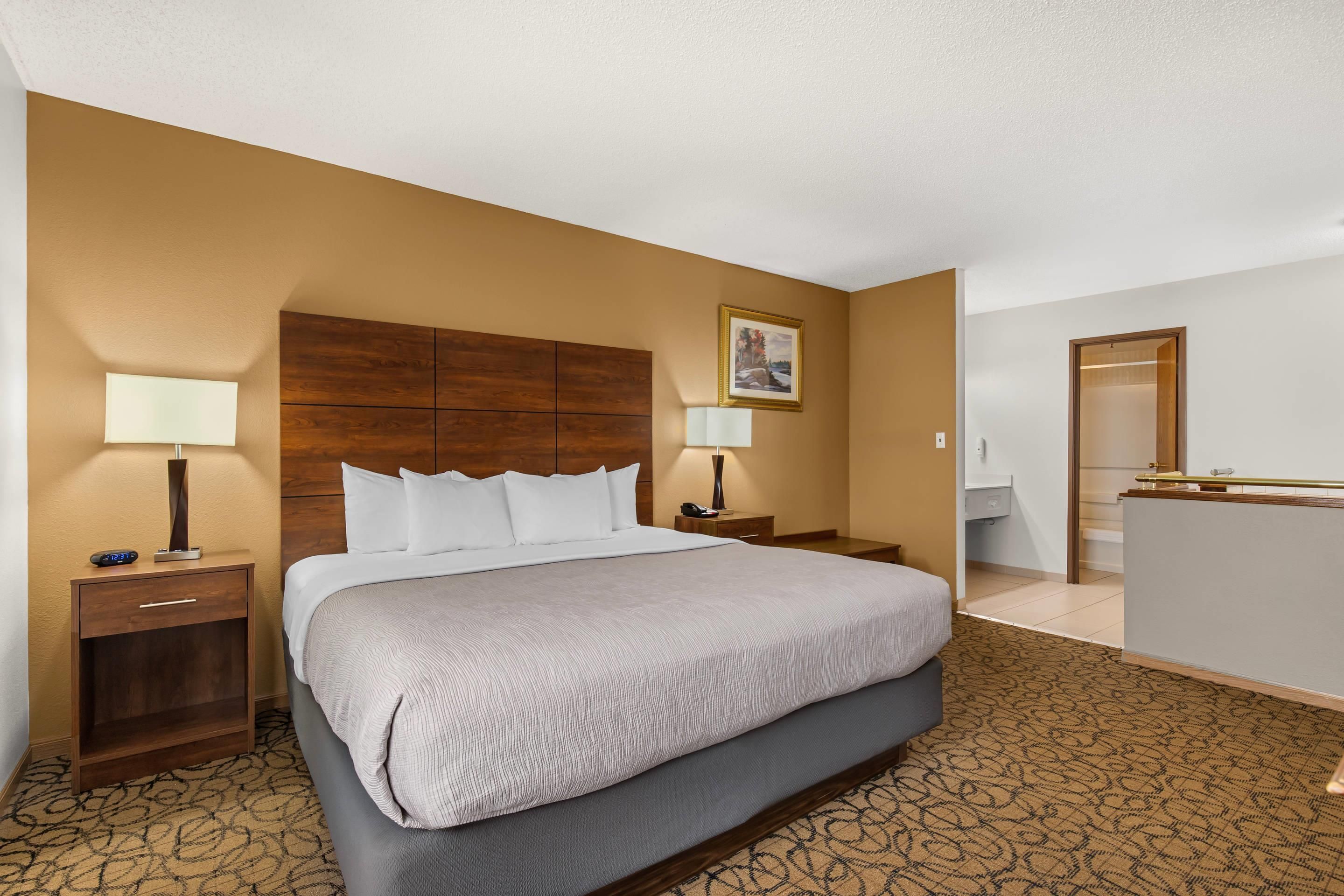 A hotel room with a large bed, two bedside tables, a desk, a chair, and a bathroom visible through an open door.