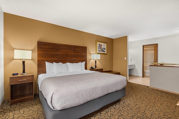 A hotel room with a large bed, two bedside tables, a desk, a chair, and a bathroom visible through an open door. - Quality Inn & Suites Manistique (Manistique)