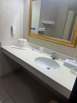 A hotel bathroom with a white sink, a mirror with a gold frame, a towel dispenser, and a soap dispenser.
