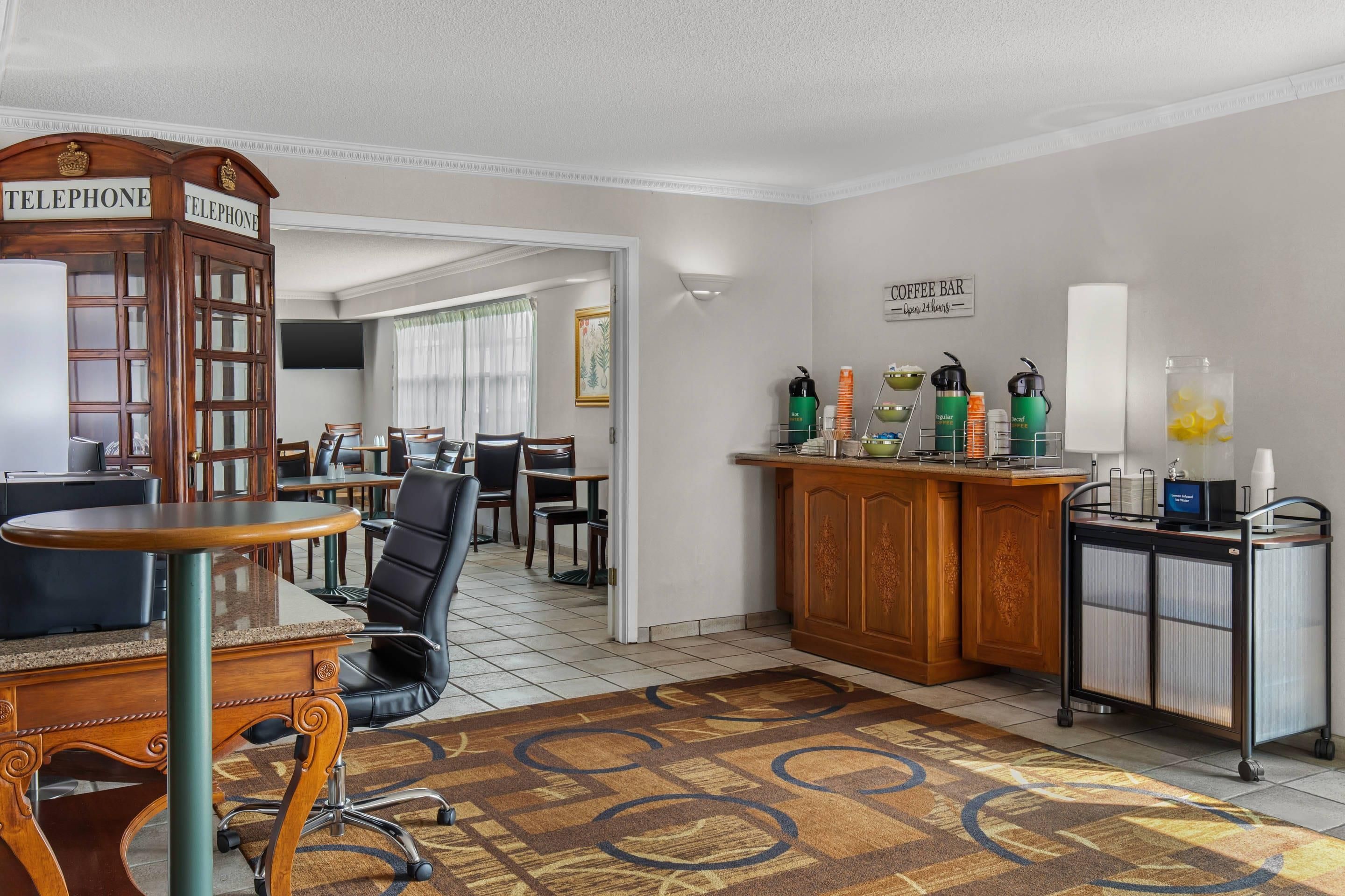 A hotel room with a dining area, a coffee bar, and a telephone booth.