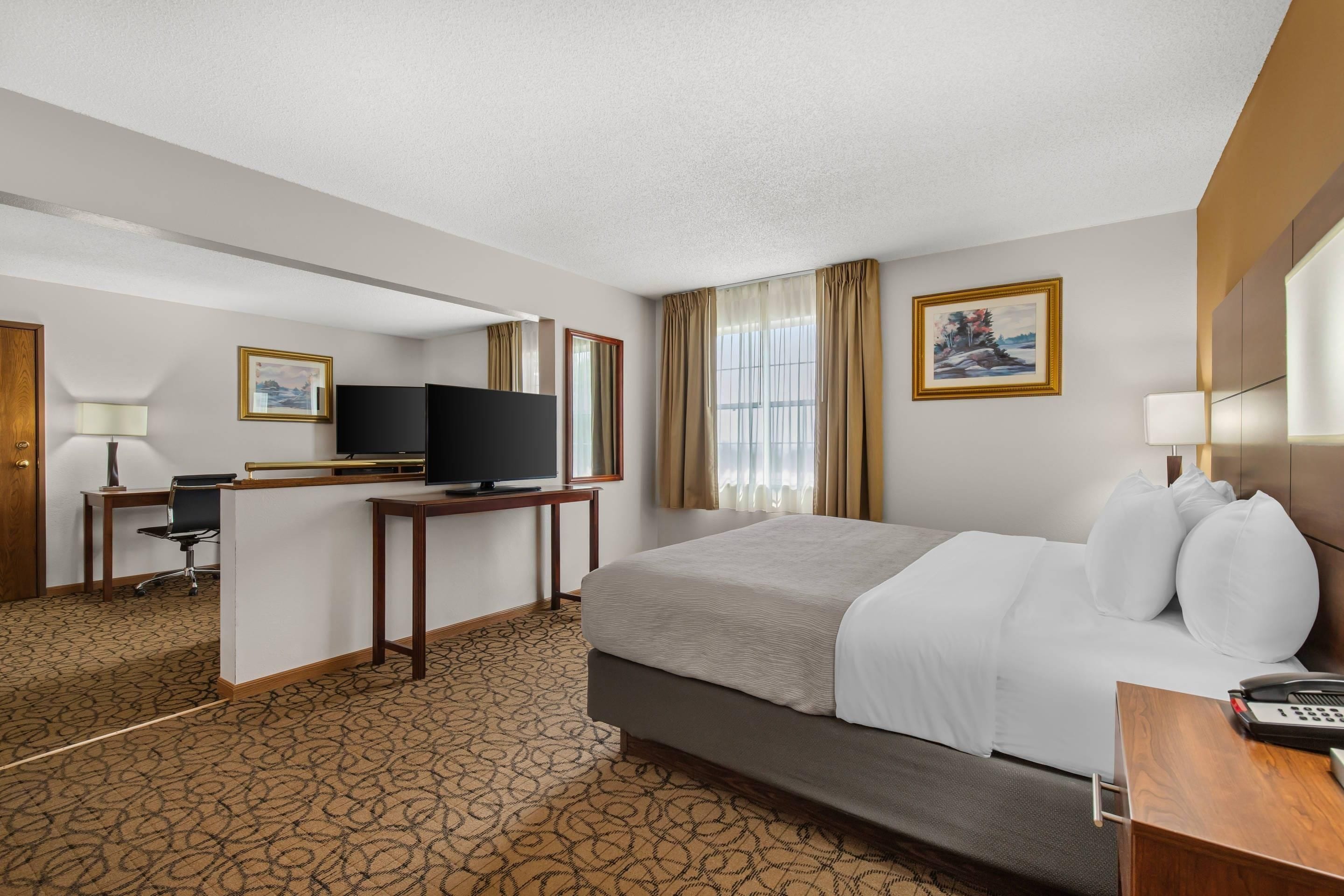 Una habitación de hotel con una cama, un escritorio con computadora, un televisor y dos cuadros en la pared.