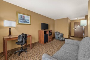 Habitación de hotel con escritorio, silla de oficina, sofá, televisión y una pequeña kitchenette.