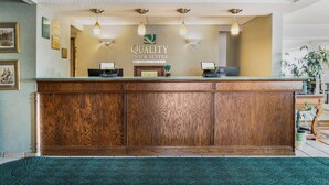 A reception desk with a wooden finish, a logo above it, and two computer monitors. - Quality Inn & Suites Manistique (Manistique)