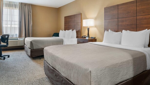 A hotel room with two beds, a desk, a chair, a lamp, and a window with curtains. - Quality Inn & Suites Manistique (Manistique)