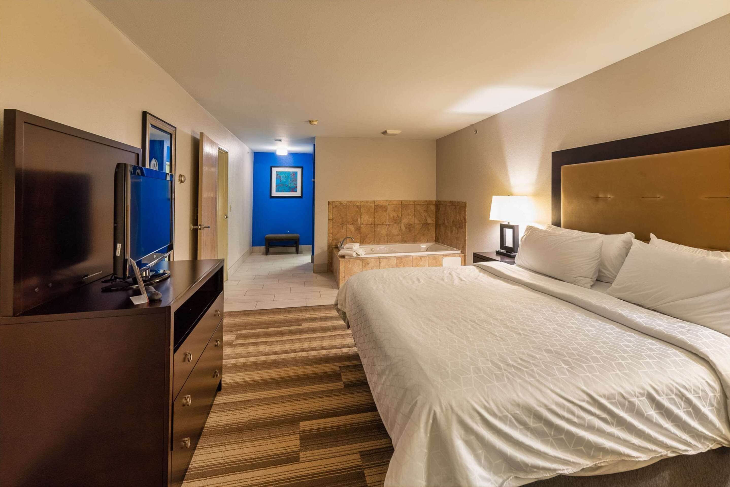 A hotel room with a bed, a TV, a bathroom with a bathtub, and a desk with a computer.