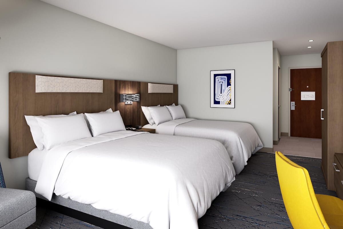 Una habitación de hotel con dos camas, cabecera de madera, una obra de arte moderna en la pared y una silla amarilla.