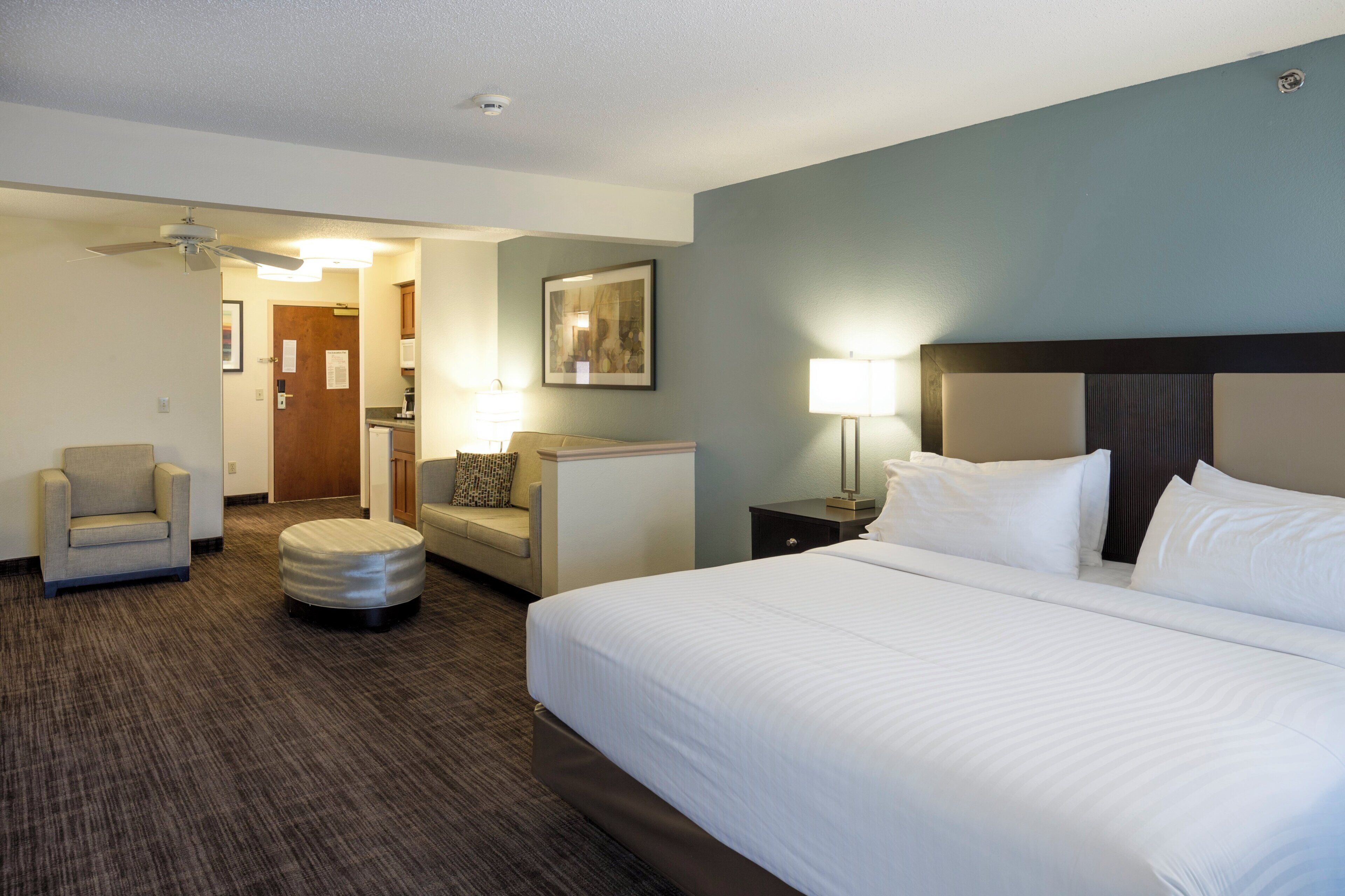 A hotel room with a large bed, a chair, a small table, a lamp, and a ceiling fan.