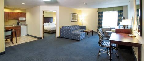 A hotel room with a kitchenette, a sofa, a desk, and a bed.