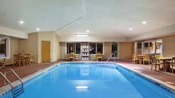 A hotel pool area with a clear blue pool, wooden chairs, and tables arranged around the pool.