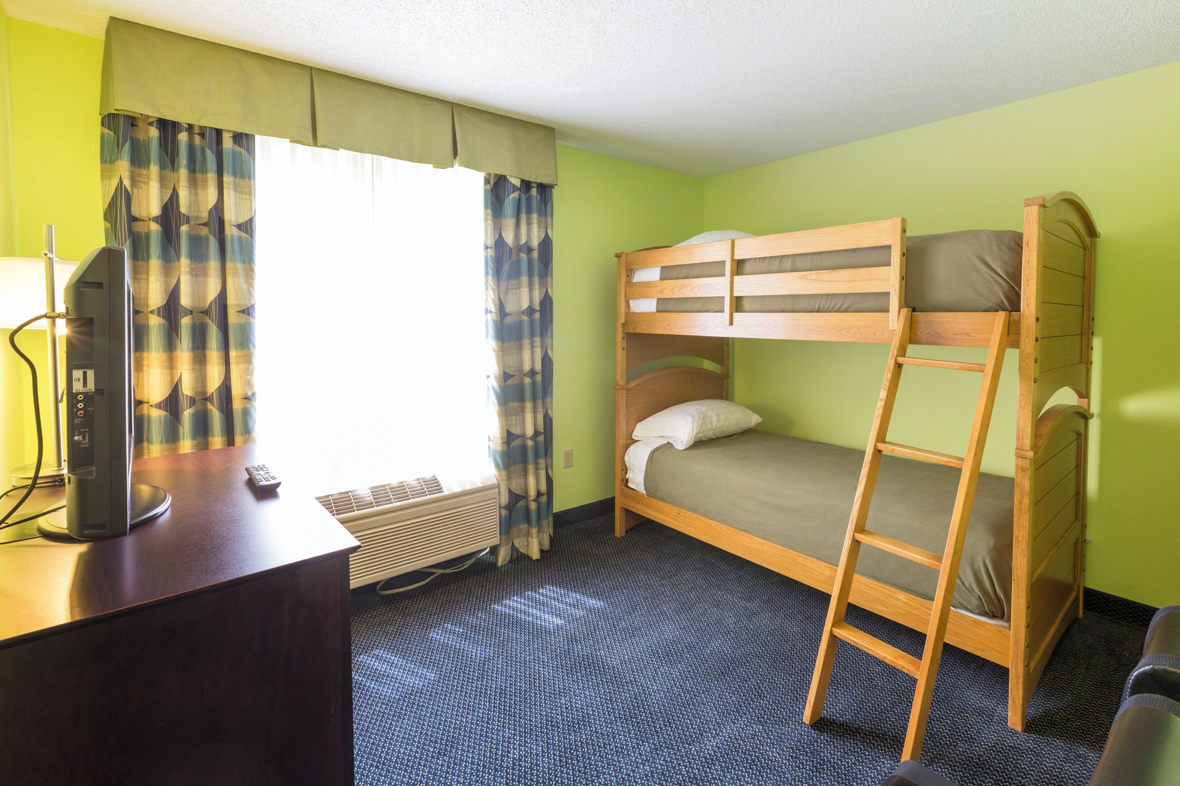 A room with a bunk bed, a desk with a computer, a chair, and a window with curtains.