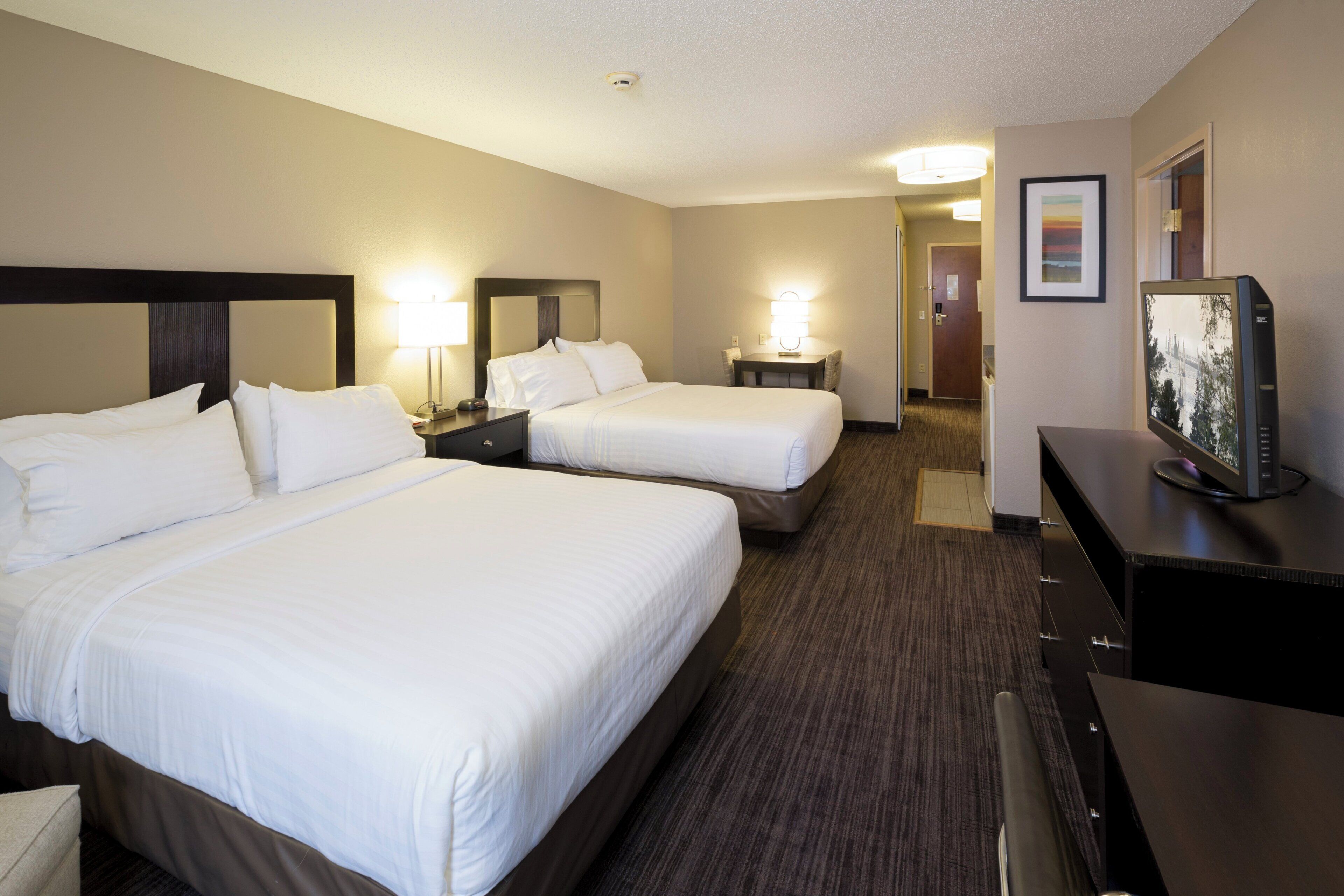 Habitación de hotel con dos camas, un escritorio con computadora y una puerta que da a otra habitación.