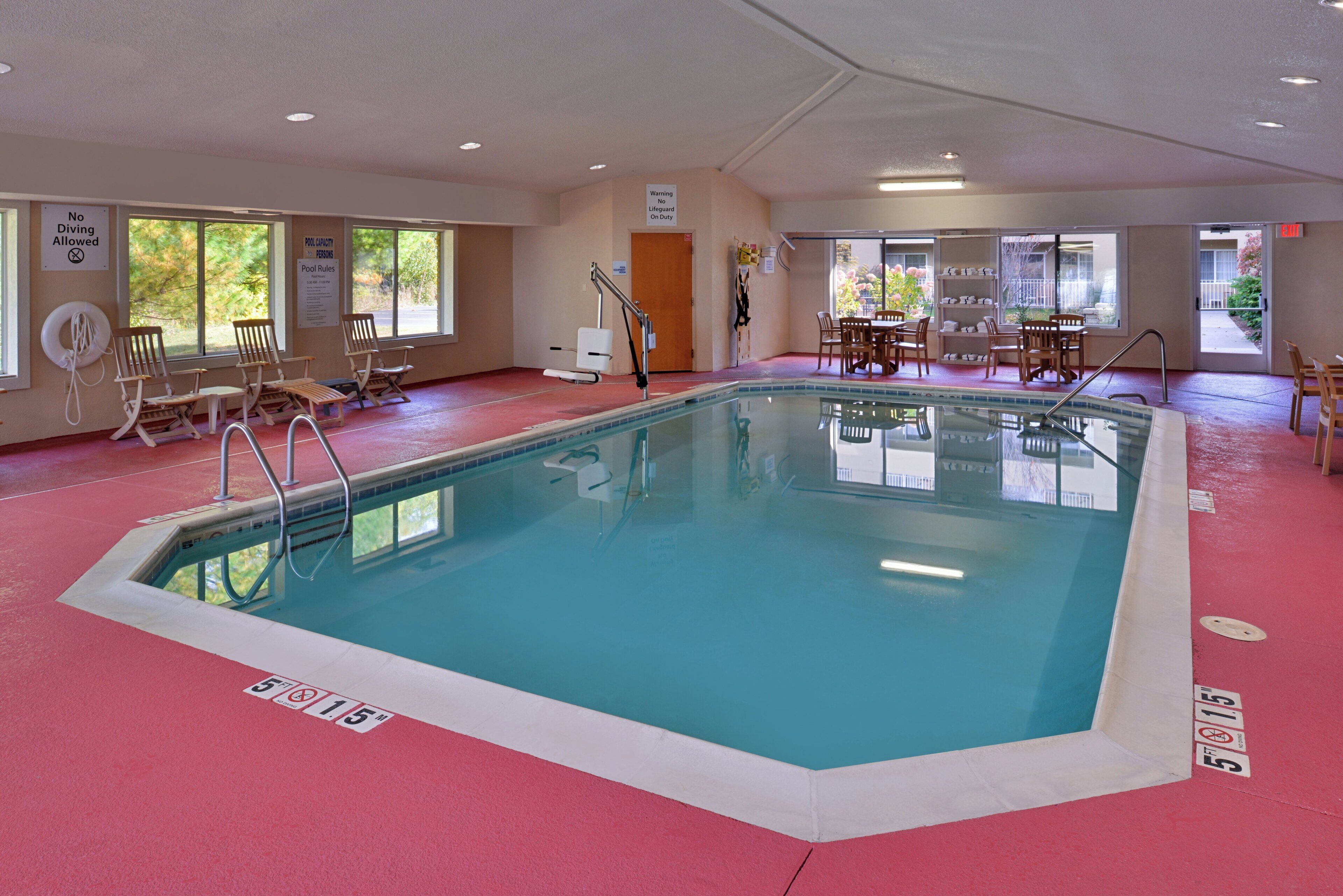An indoor swimming pool with a 5 ft depth limit, surrounded by lounge chairs and a table with chairs.