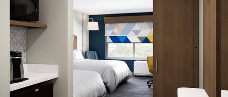 A hotel room with a bed, a desk, a chair, a TV, and a window with a geometric curtain.