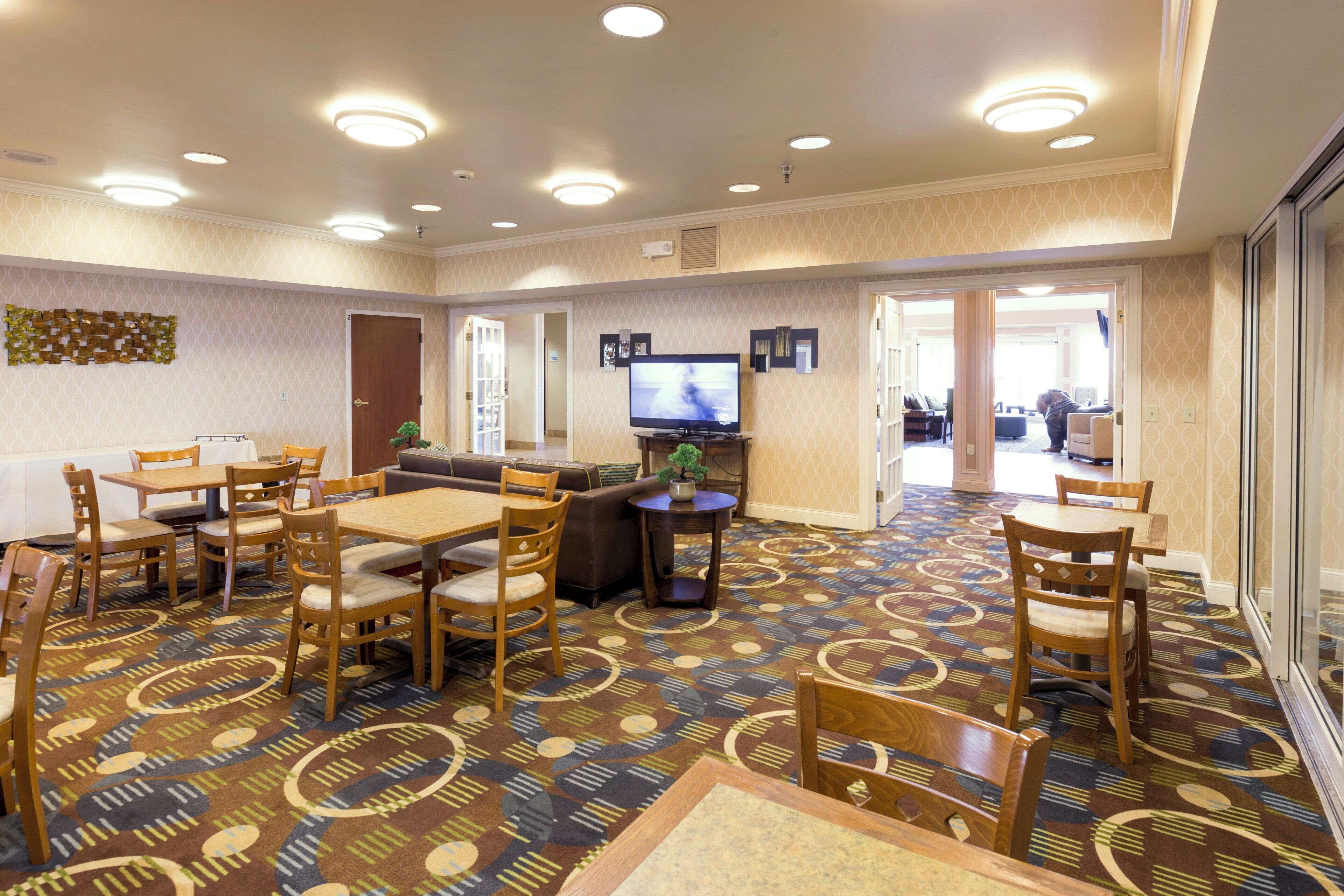 A hotel room with a dining area, a television, and a patterned carpet.