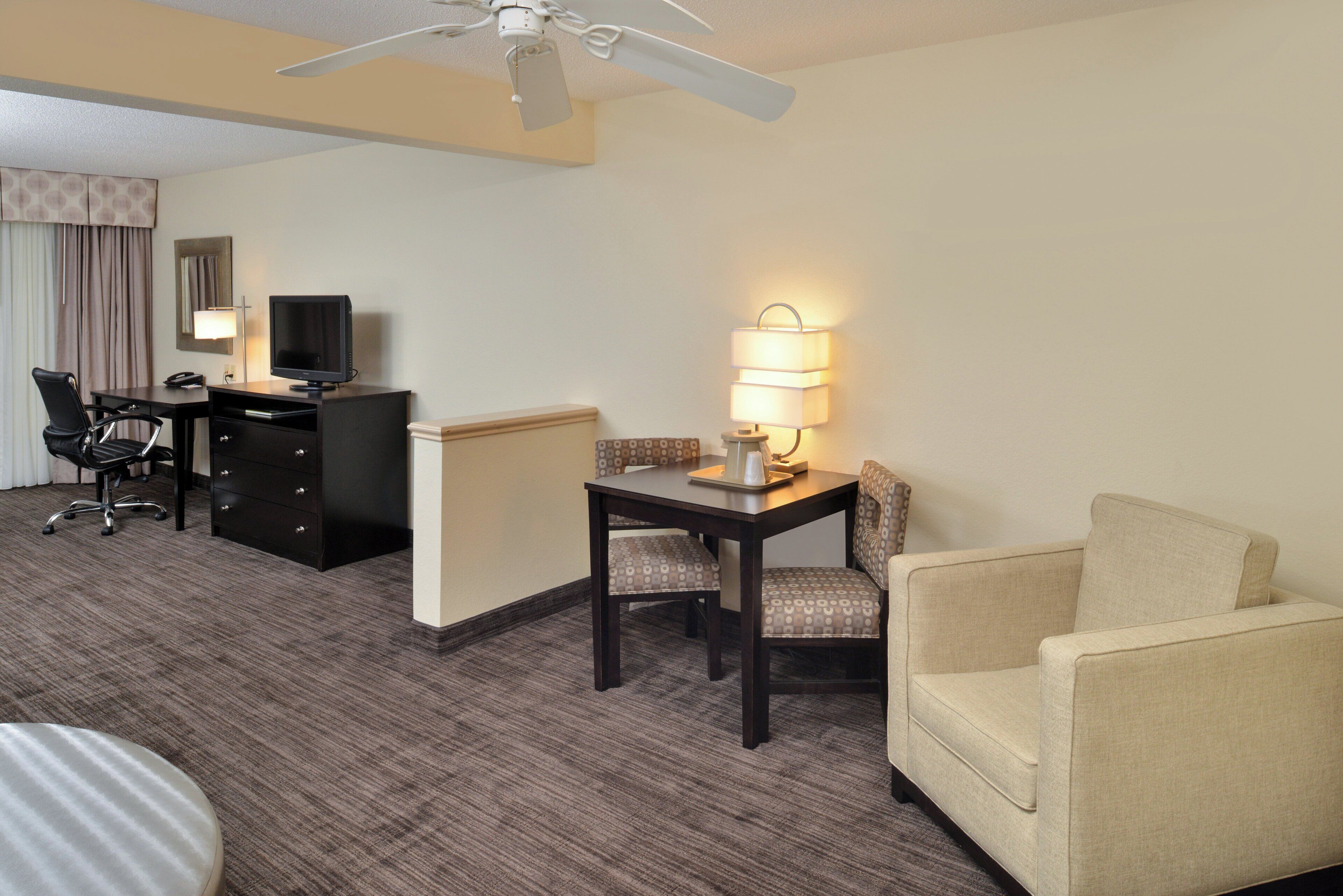Habitación de hotel con escritorio, televisor, lámpara, sofá y ventilador de techo.