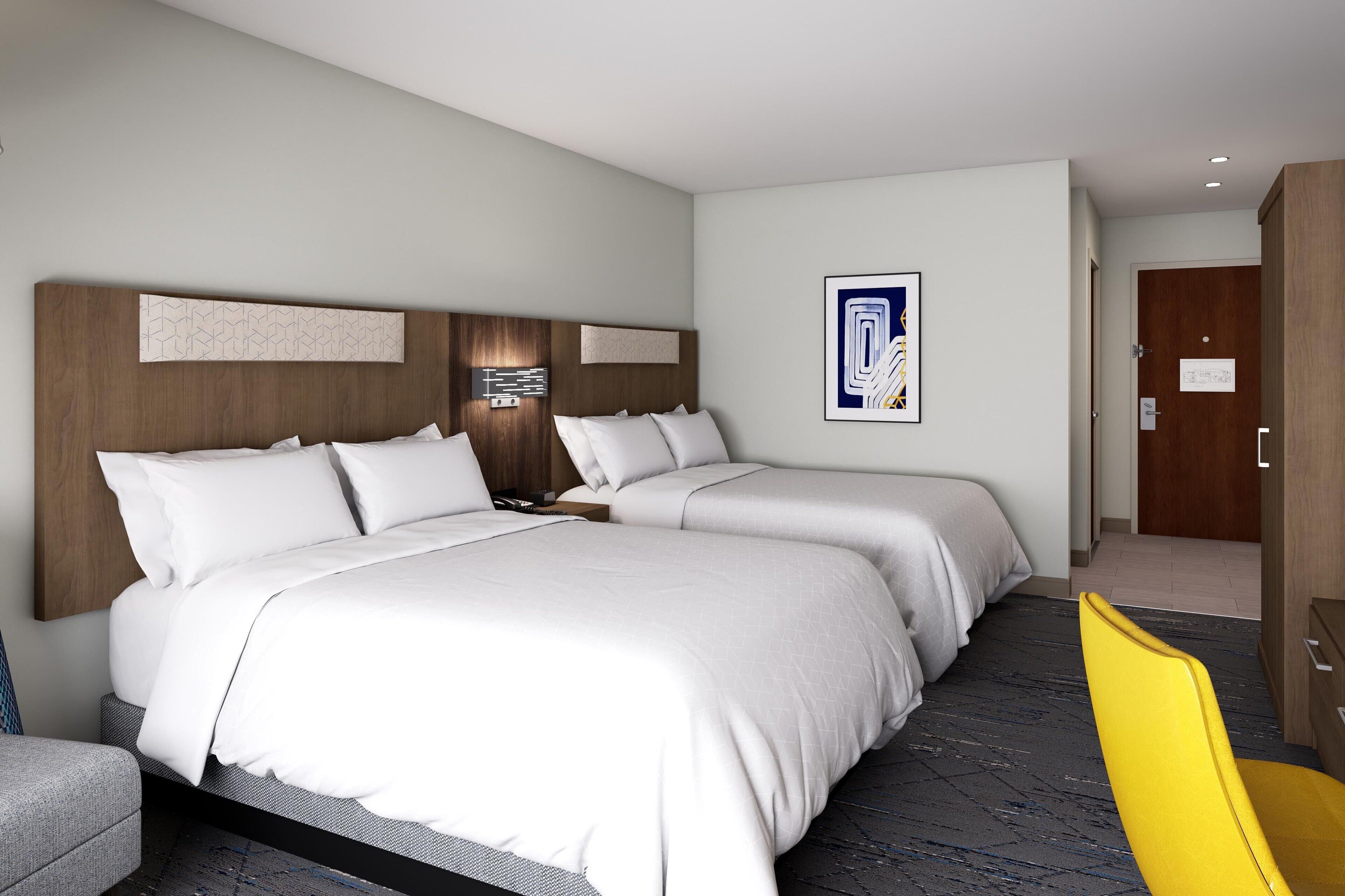 A hotel room with two beds, a wooden headboard, a modern wall art piece, and a yellow chair.