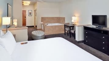 A hotel room with a large bed, a desk with a chair, a television, a bathroom with a bathtub, and a ceiling fan.