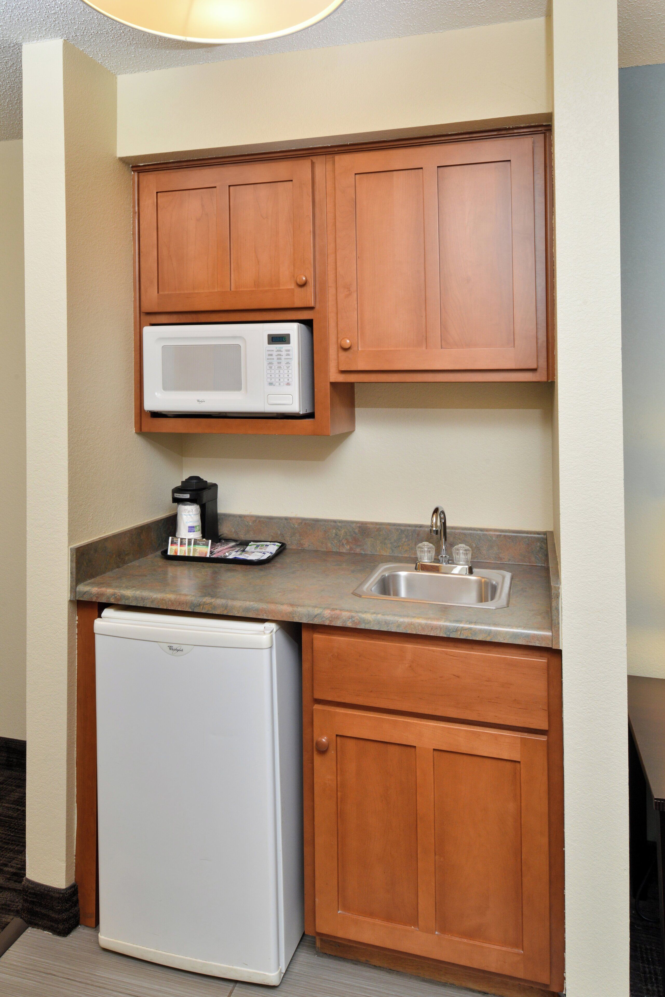 Una kitchenette compacta con microondas, cafetera y refrigerador pequeño.