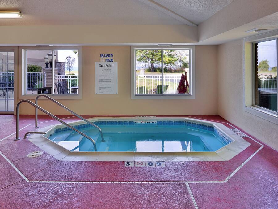 A swimming pool with a red textured floor, a metal ladder, and a sign indicating a spa capacity of 12 persons.