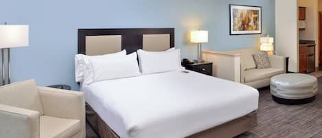 A hotel room with a large bed, a chair, a desk, a lamp, and a painting on the wall.